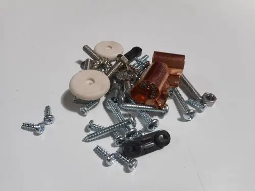 Schnapsglas mit verschiedenen Schrauben und Metallteilen, darunter einige Remeha-Komponenten, auf einer hellen Oberfläche.